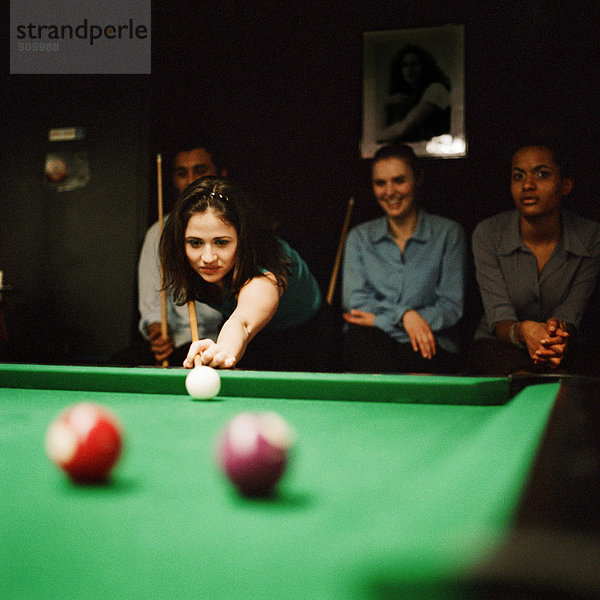 Junge Frau beim Billard spielen  junge Leute sitzen im Hintergrund