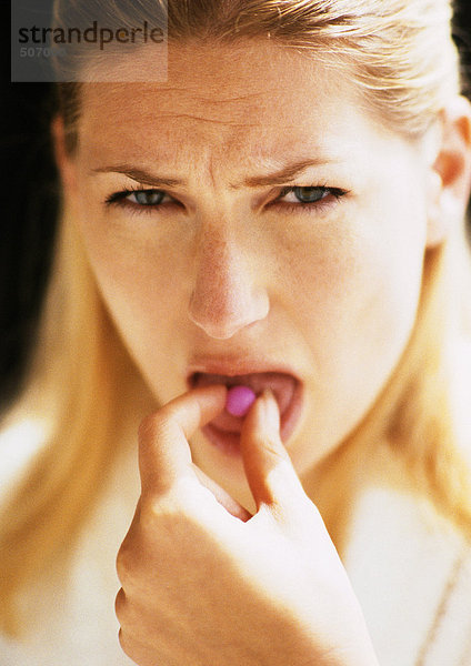 Eine Frau steckt die Pille in den Mund  schaut in die Kamera.