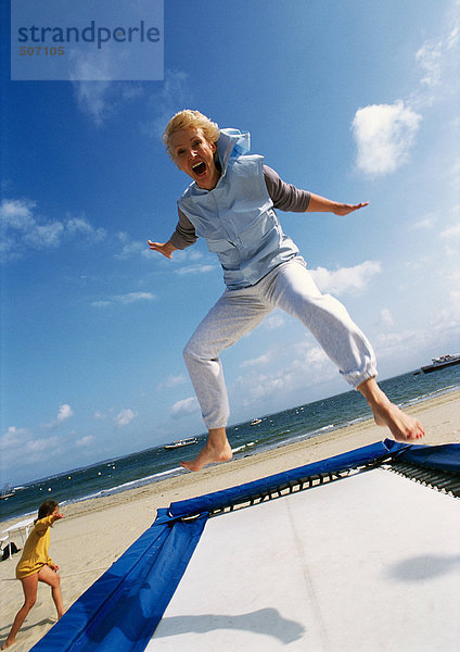 Reife Frau beim Springen auf Trampolin am Strand