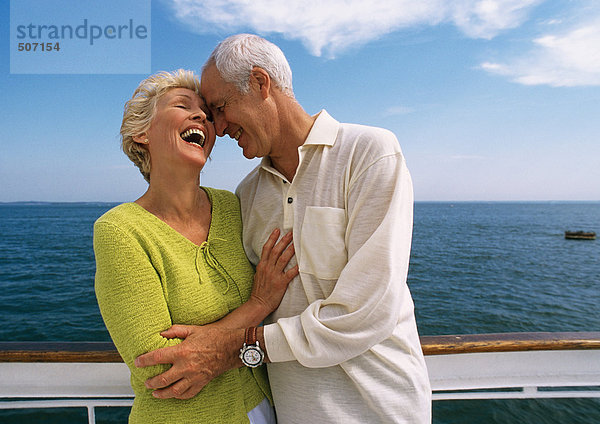 Ein reifes Paar umarmt sich  lacht auf dem Bootsdeck.