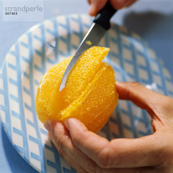 Nahaufnahme der Hände  die mit einem Messer geschältes Orange schneiden.
