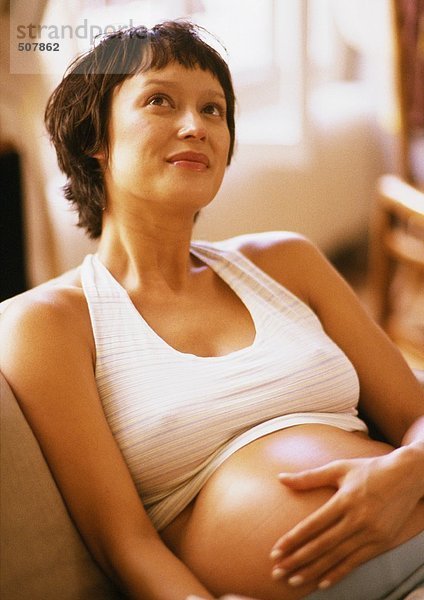 Schwangere Frau im Sessel  Hand auf dem Bauch und aufblickend