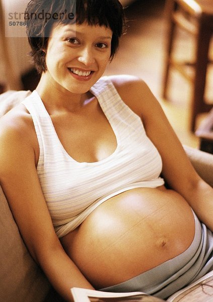 Schwangere Frau im Sessel sitzend  lächelnd vor der Kamera  Porträt