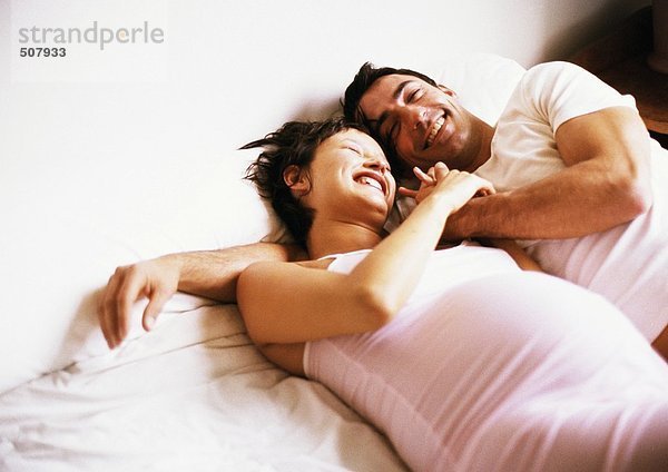 Mann und schwangere Frau Seite an Seite auf dem Bett