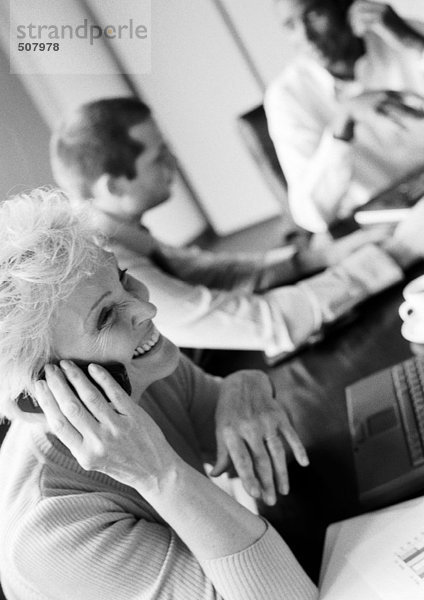 Businesswoman using cell phone in conference room  colleagues in blurred background  B&W