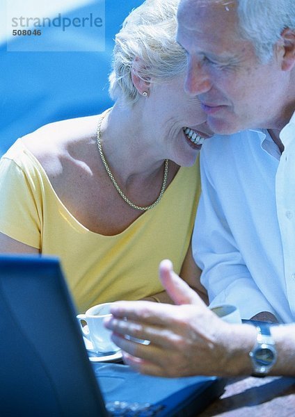 Reife Frau und Mann im Freien sitzend mit Laptop-Computer