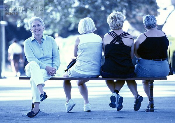 Vier Frauen sitzen auf einer Bank  drei von hinten gesehen