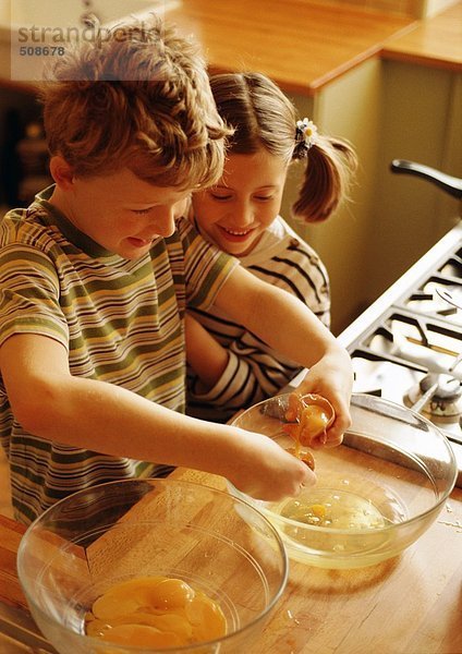 Zwei Kinder lächeln in der Küche mit einer Schüssel Eigelb und einer Schüssel Eiweiß.