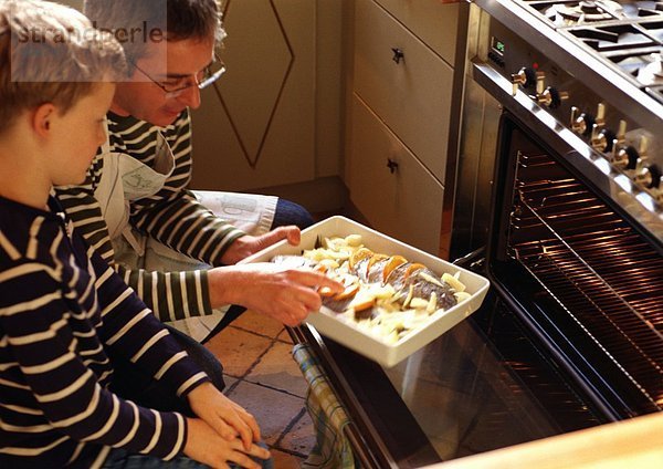Mann und Kind stellen Kasserolle in den Ofen