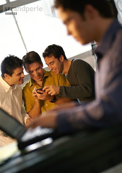 Drei Männer schauen auf Handheld-Computer  vierter Mann mit Laptop im Vordergrund