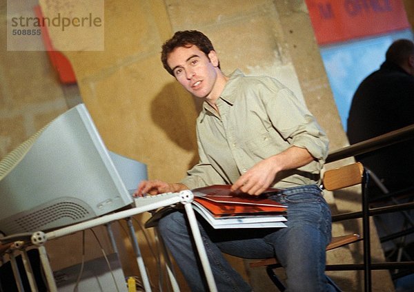Mann vor dem Computer sitzend mit Buch auf Knien  Portrait