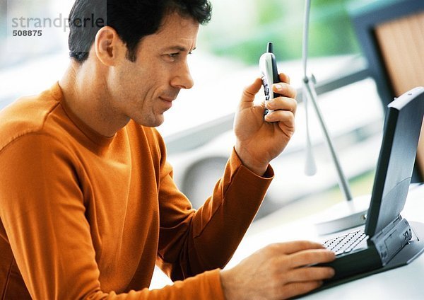 Mann hält Handy  schaut auf Laptop-Computer