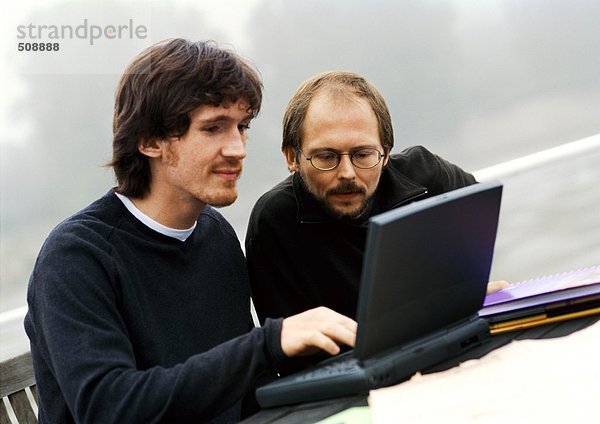Zwei Männer arbeiten im Freien am Laptop.