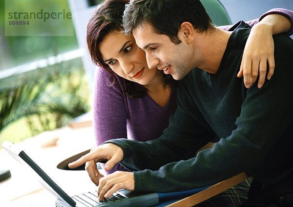 Mann mit Laptop-Computer  Frau mit Arm um ihn herum sitzend
