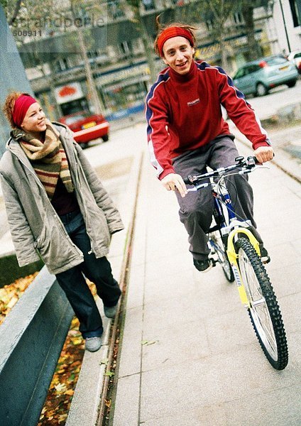Zwei Jugendliche auf dem Bürgersteig  einer auf dem Fahrrad