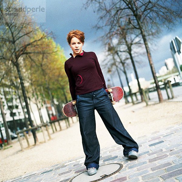 Junge Frau hält ein Skateboard hinter sich  Porträt