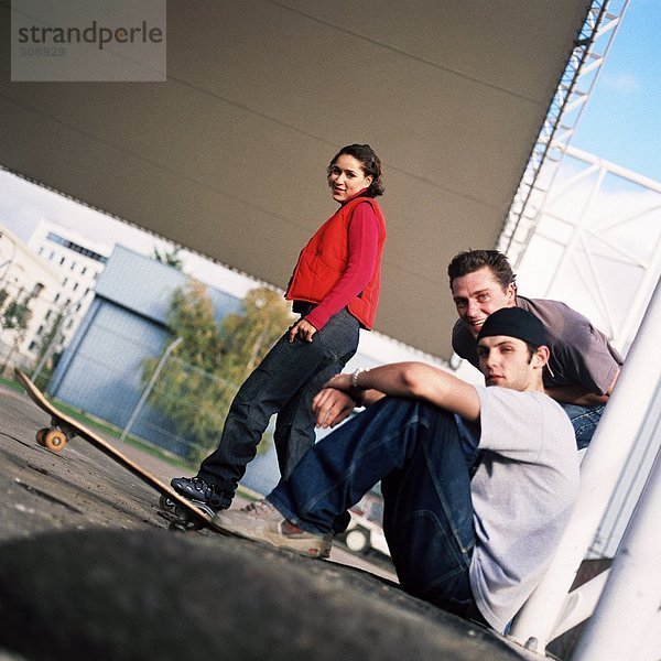 Drei Jugendliche  einer mit Skateboard  Seitenansicht  Portrait