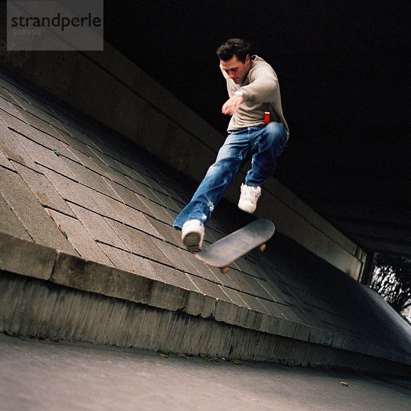 Junger Mann im Luftsprung mit Skateboard