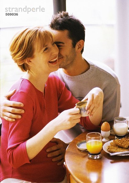 Schwangere Frau und Mann beim Frühstücken  lächelnd