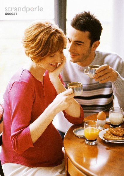 Schwangere Frau und Mann beim Frühstücken  lächelnd