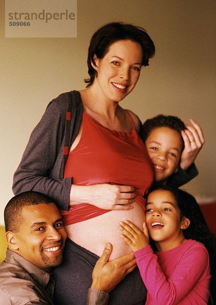 Mann und Kinder um den exponierten Bauch der Schwangeren herum