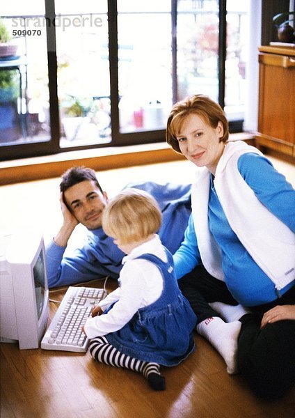Schwangere Frau und Mann auf dem Boden mit Kind berührt Computer-Tastatur