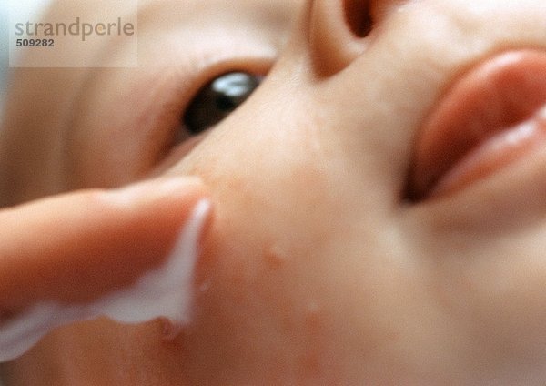 Baby mit Lotion  die auf das Gesicht aufgetragen wird  extreme Nahaufnahme