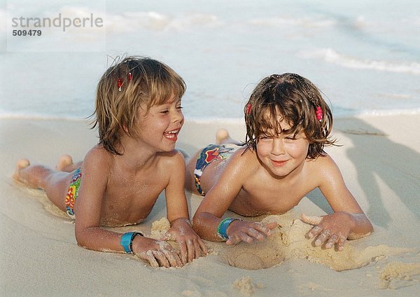 Zwei Mädchen auf Sand am Strand liegend  lächelnd