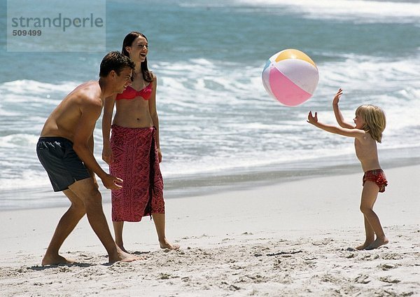 Junge Familie spielt mit Strandball am Strand