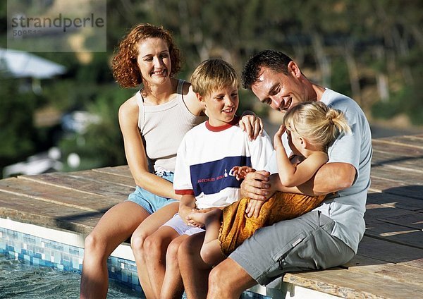 Junge Familie  gekleidet  am Rande des Pools sitzend.