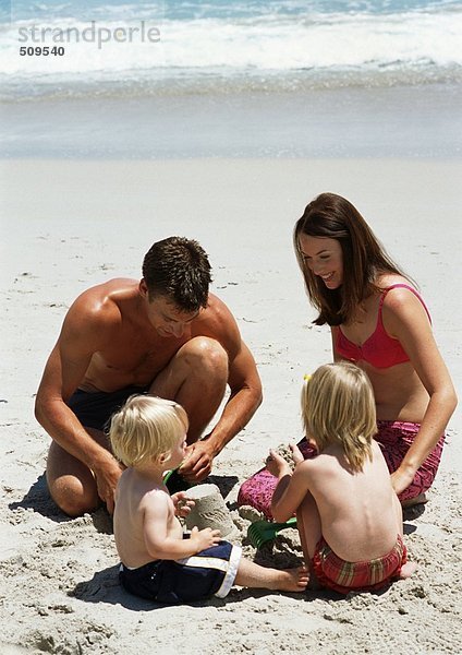 Junge Familie beim Bau einer Sandburg am Strand