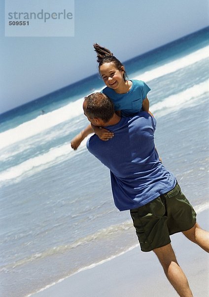 Mann  der ein junges Mädchen am Strand trägt.