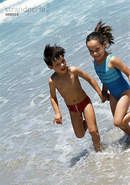 Zwei Kinder halten sich im Wasser am Strand an den Händen.