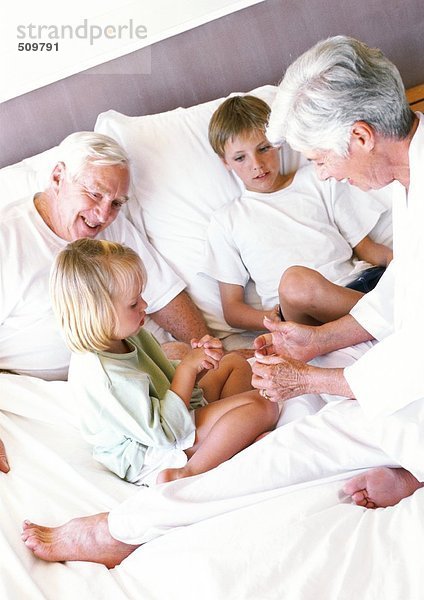 Großeltern und Kinder auf dem Bett sitzend