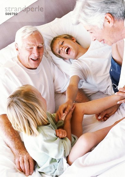 Großeltern und Kinder  die auf dem Bett spielen  lächelnd