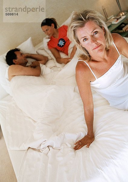 Frau auf dem Bett sitzend  Familie im Bett liegend im Hintergrund