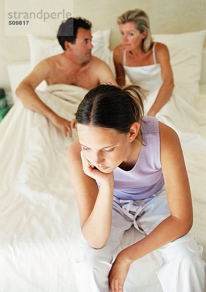 Teenagermädchen auf dem Bett der Eltern sitzend  Kopf haltend  Eltern im Hintergrund  Hochwinkelansicht