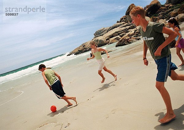 Junge Leute spielen Fußball am Strand