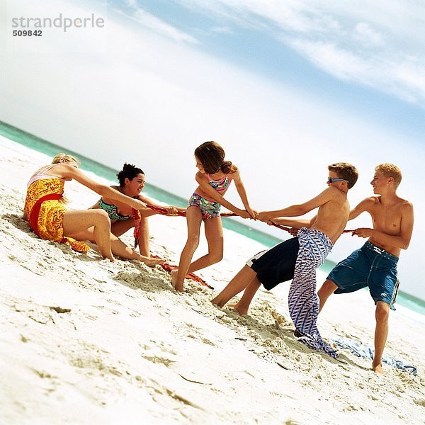 Eine Gruppe von Leuten  die am Strand Tauziehen spielen.