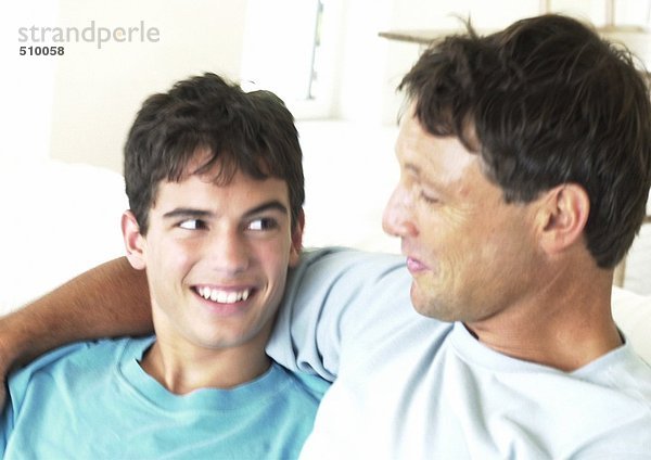 Vater und Teenager lächeln sich an  der Arm des Mannes um den Jungen.