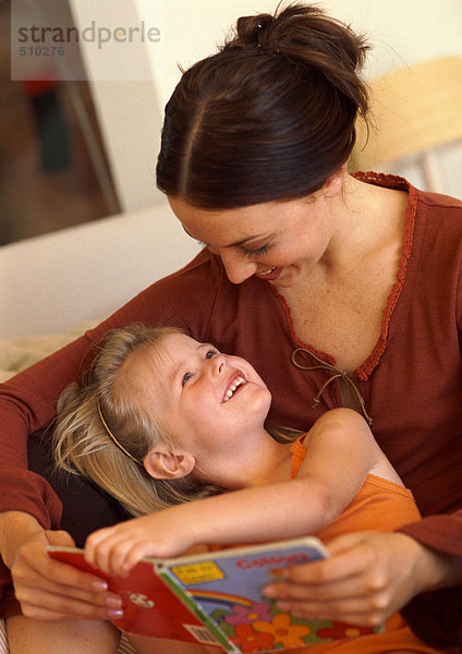 Mutter und Tochter lesen Buch  lächelnd