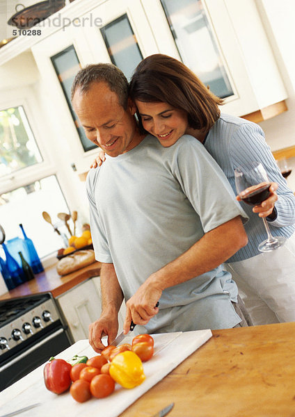 Paar in der Küche  Mann schneidet Gemüse  während die Frau dem Mann über die Schulter schaut.