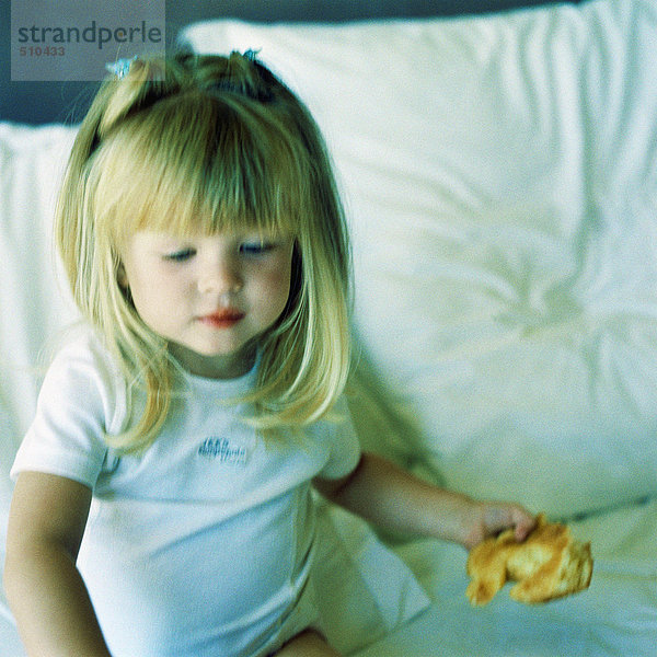 Mädchen auf dem Bett sitzend  Croissant haltend