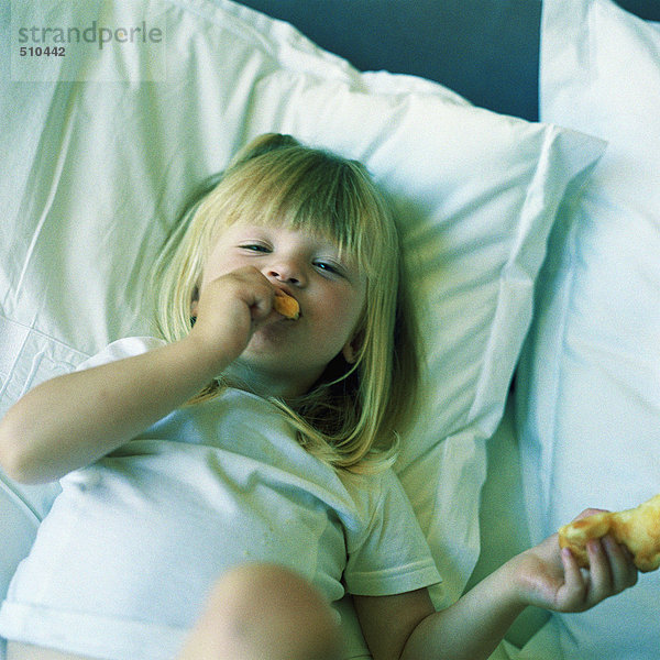 Kind auf dem Bett liegend  essend