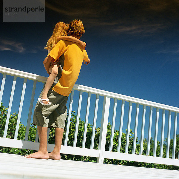 Junge hält kleines Mädchen am Geländer  Rückansicht