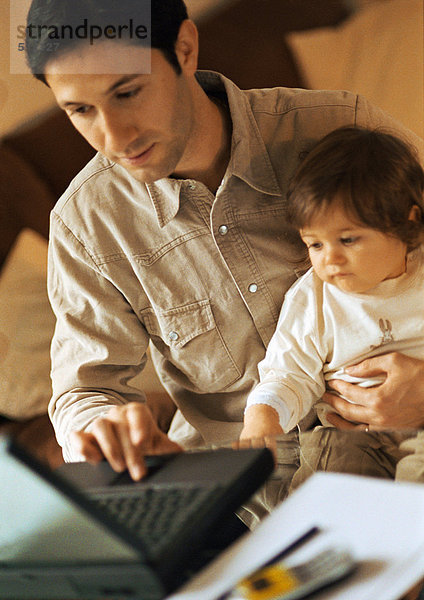 Vater und Baby  Vater mit Laptop  Baby sitzt auf Vaters Schoß.