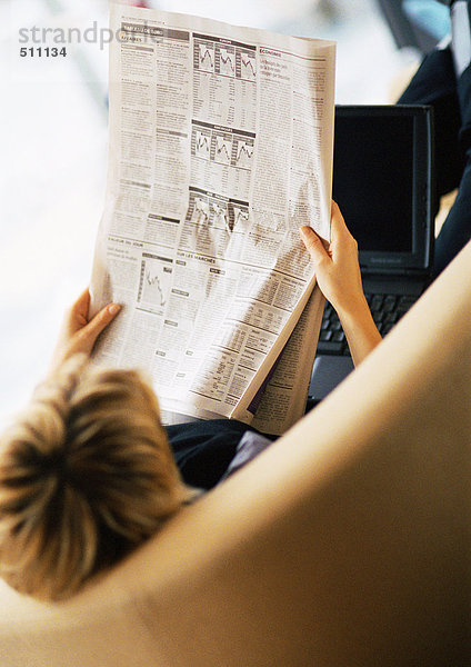 Frau liest Zeitung  Laptop auf dem Schoß  Rückansicht  erhöhter Winkel.