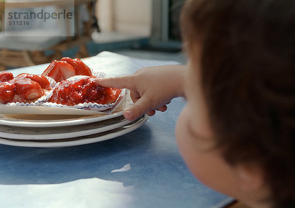 Kleines Kind mit dem Finger auf dem Kuchen  Konzentration auf die Hand.