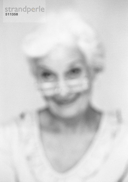 Seniorin mit Blick über den Brillenrand  Nahaufnahme  Portrait  verschwommen  s/w