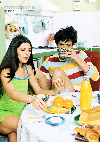Ein junges Paar sitzt am Tisch und frühstückt.